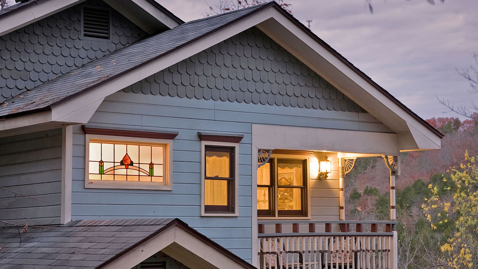 The bed and breakfast has a gently sloping roof, a hallmark of Craftsman homes. Backlight with interior lighting at dusk.
