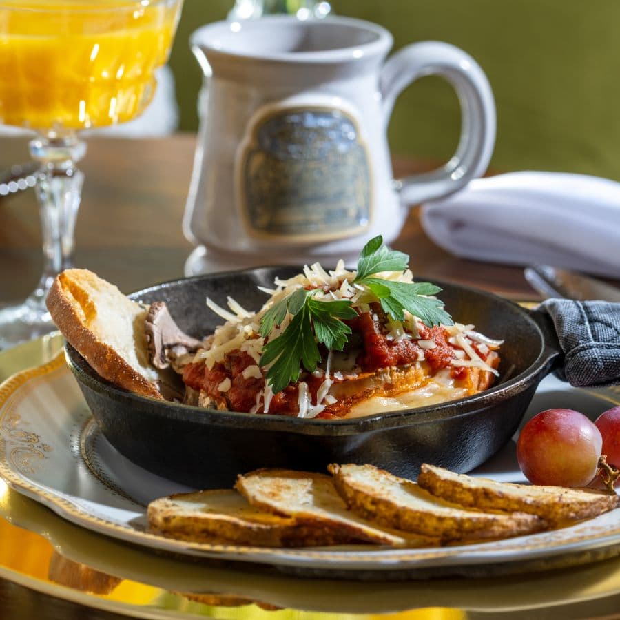 Savory breakfast dish in a cast iron pan with toast slices, grapes, glass of orange juice and a ceramic coffee mug